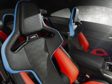 Close-up van sportieve BMW M4 Competition x KITH autostoelen met zwarte, rode en blauwe details in een modern voertuiginterieur.