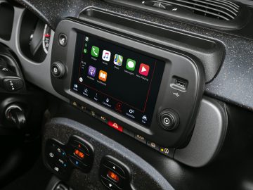 Autodashboard met een modern infotainmentscherm met app-pictogrammen, omgeven door airconditioningbedieningen en gestructureerde panelen in een Fiat Panda Sport.