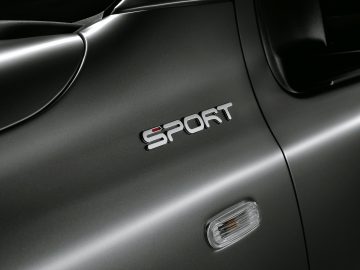 Close-up van het zijpaneel van een grijze Fiat Panda Sport met een 'sport'-badge en een richtingaanwijzer aan de zijkant.