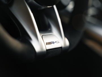 Close-up van het AMG-logo op het stuur van een Mercedes-AMG GT C Roadster, waarbij de details en textuur van het stuur centraal staan.