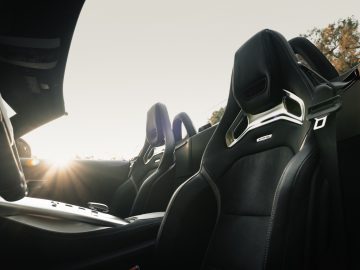 Binnenaanzicht van een Mercedes-AMG GT C Roadster met twee leren stoelen, met de zonsondergang zichtbaar op de achtergrond.