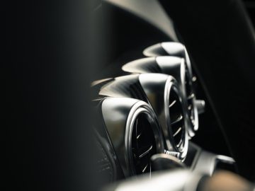 Close-up van het interieur van een Mercedes-AMG GT C Roadster, waarbij het stuur en het dashboard met ronde ventilatieopeningen centraal staan, verlicht door natuurlijk licht.