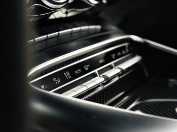 Close-up van het klimaatbeheersingssysteem van een Mercedes-AMG GT C Roadster met temperatuur- en ventilatorsnelheidswijzerplaten, geplaatst in een metalen dashboard.