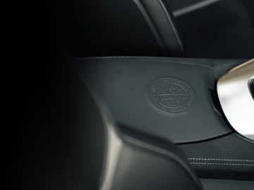 Close-up van de leren stoel van een Mercedes-AMG GT C Roadster met een logo in reliëf op de hoofdsteun, met een wazig stuur op de voorgrond.