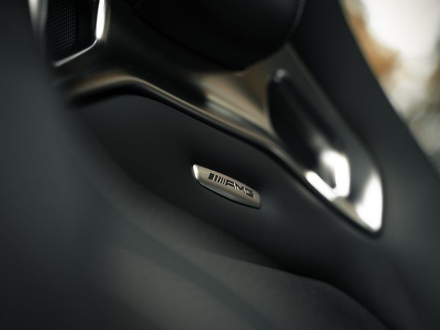 Close-up van het interieur van een auto met het Mercedes-AMG GT C Roadster-embleem op een deurklink, met een softfocusachtergrond.