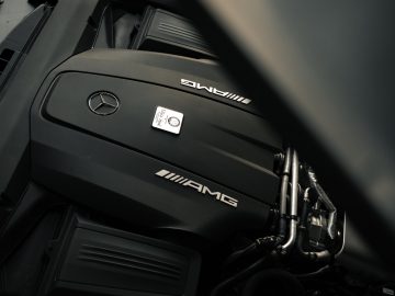 Close-up van de motorruimte van een Mercedes-AMG GT C Roadster, met de motorkap met het Mercedes-logo en AMG-logo.