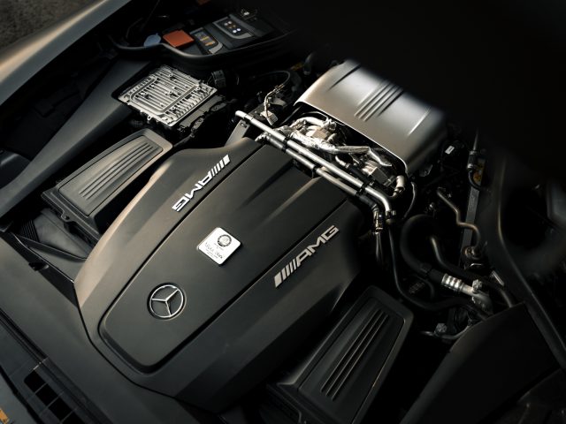 Gedetailleerd overzicht van de motorruimte van een Mercedes-AMG GT C Roadster, met de nadruk op de slanke, metalen kap en ingewikkelde componenten.