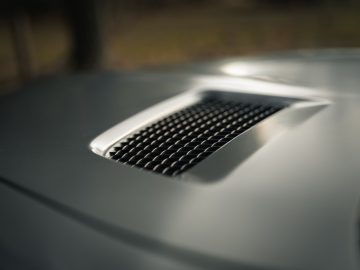 Close-up van de motorkap van een Mercedes-AMG GT C Roadster met een gedetailleerde ventilatieopening, gericht op de zwarte mesh-grille tegen een onscherpe achtergrond.