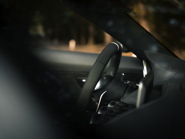 Binnenaanzicht van een Mercedes-AMG GT C Roadster, gefocust op het stuur en het dashboard, met een wazige bosachtergrond gezien door de voorruit.