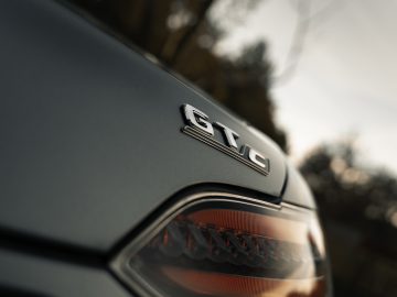 Close-up van de achterkant van een Mercedes-AMG GT C Roadster met een 'gtc'-badge op een matte afwerking met een onscherpe natuurlijke achtergrond.