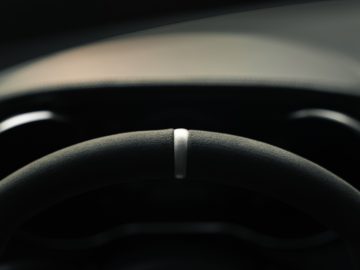 Close-up van een Mercedes-AMG GT C Roadster-stuur met focus op het logo in het midden, tegen een donkere dashboardachtergrond.