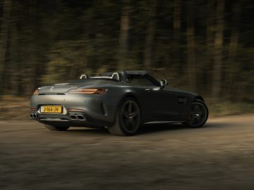 Een zwarte Mercedes-AMG GT C Roadster die over een bosweg snelt, in beweging vastgelegd met een onscherpe achtergrond.