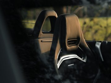 Binnenaanzicht van een Mercedes-AMG GT C Roadster met twee lederen stoelen met hoofdsteunen, stuur en een open dak, omlijst door een gedeeltelijk zichtbaar raam.