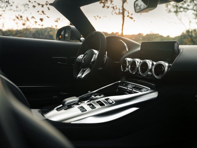 Binnenaanzicht van een moderne Mercedes-AMG GT C Roadster bij zonsondergang, met een stijlvol dashboard, lederen stoelen en een digitaal display.