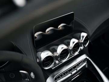 Close-up van de ventilatieopeningen en het multimediascherm van een Mercedes-AMG GT C Roadster op een dashboard met koolstofvezelaccenten.