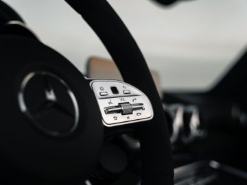 Close-up van een Mercedes-AMG GT C Roadster-stuur met bedieningsknoppen voor volume, telefoon en andere voertuigfuncties.