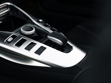 Close-up van de middenconsole van de Mercedes-AMG GT C Roadster met metallic accenten, met versnellingspook, bedieningsknoppen en knoppen.