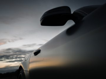 Zijaanzicht van een Mercedes-AMG GT C Roadster, waarbij de achteruitkijkspiegel en de carrosseriecurven tegen een schemerige hemel worden benadrukt.
