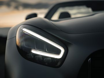 Close-up van de LED-koplamp van een Mercedes-AMG GT C Roadster met een wazige zonsondergang op de achtergrond, wat het strakke design van de auto benadrukt.