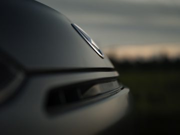 Close-up van de motorkap en grille van een Mercedes-AMG GT C Roadster in de schemering, waarbij de lijnen en het embleem van de auto centraal staan, met een softfocusachtergrond van een schemerige lucht.