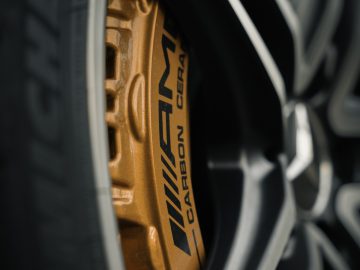 Close-up van de lichtmetalen velg van een Mercedes-AMG GT C Roadster met een gouden remklauw met daarop 'koolstofkeramiek' geschreven, afgezet tegen een zwart wiel en band.