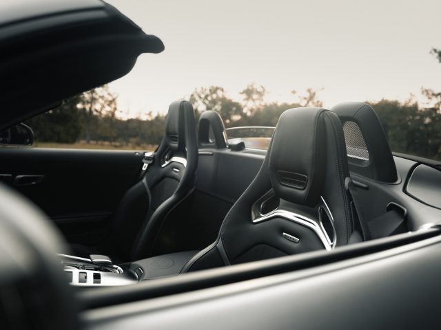 Binnenaanzicht van de Mercedes-AMG GT C Roadster met open dak, met leren stoelen en modern dashboard in de schemering.