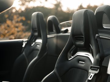 Binnenaanzicht van een Mercedes-AMG GT C Roadster met zwartleren stoelen met de nadruk op de voorstoelen en een onscherpe natuurlijke achtergrond.