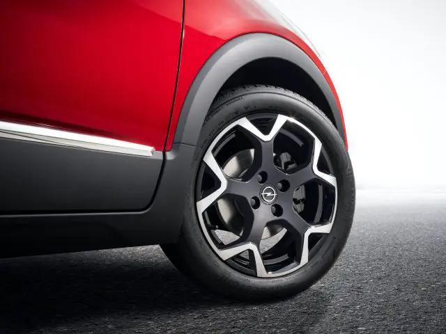 Close-up van het achterwiel en spatbord van een rode Opel Crossland, met een glanzende lichtmetalen velg met een logo, geparkeerd op een betonnen oppervlak.