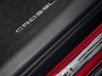 Close-up van de dorpel van een auto met het Opel Crossland-logo op een chromen strip en 'Crossland' in reliëf op het zwarte oppervlak erboven.