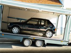 Een zwarte Peugeot-auto die overdag op de achterkant van een open, witte transporttrailer werd geladen.