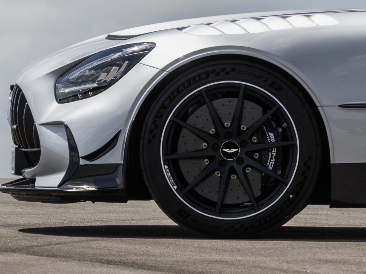 Close-up van een zilveren Aston Martin, met de linkervoorband en een deel van de gestroomlijnde motorkap, waarbij de zwarte velg en de laagprofielband benadrukt worden.