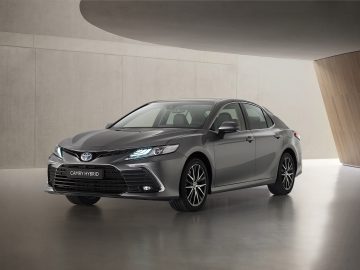 Een grijze Toyota Camry geparkeerd in een moderne betonnen binnenruimte, waar het strakke ontwerp en de hybridetechnologie goed tot hun recht komen.