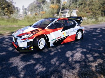 Een Toyota GR Yaris Rally Concept, versierd met sponsoring van Microsoft, navigeert over een gebogen grindweg omringd door groene bomen en struiken onder een heldere hemel.