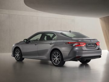 Een Toyota Camry hybride geparkeerd in een moderne betonnen showroom, met een strak achterprofiel en lichtmetalen velgen.