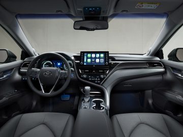 Binnenaanzicht van een Toyota Camry met een stuur met bedieningselementen, een groot touchscreen op het dashboard en lederen stoelen.