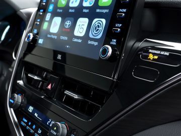 Binnenaanzicht van een Toyota Camry met een groot touchscreen-dashboard met verschillende apps zoals kaarten, telefoon en berichten, met daaronder de klimaatknoppen.