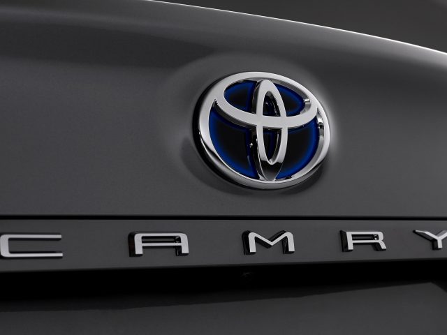 Close-up van een Toyota Camry-embleem op een grijze auto-oppervlak.