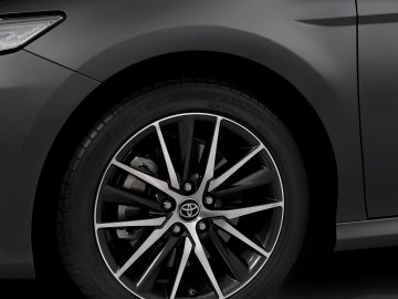 Close-up van een grijze lichtmetalen Toyota Camry-velg met een glanzende zwarte band, met een opvallend zilverkleurig logo in het midden.