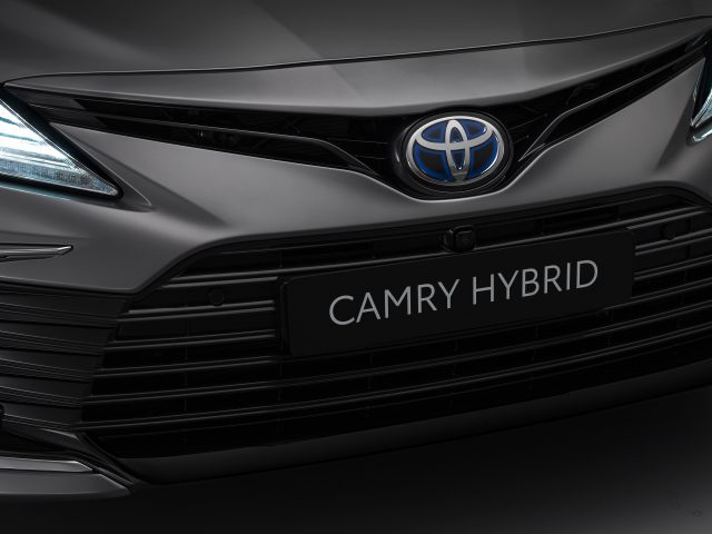 Close-up van de grille en het embleem van een Toyota Camry, waarbij het strakke ontwerp en de dagrijverlichting worden benadrukt.