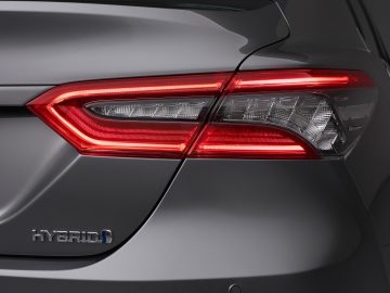 Close-up van het achterlicht en de kofferbak van een grijze Toyota Camry hybride auto met een "hybride" badge zichtbaar.