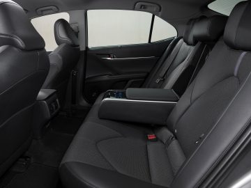 Binnenaanzicht van de achterbank van een Toyota Camry met zwarte bekleding, voorzien van een armleuning en digitale bedieningselementen op de zijdeur.