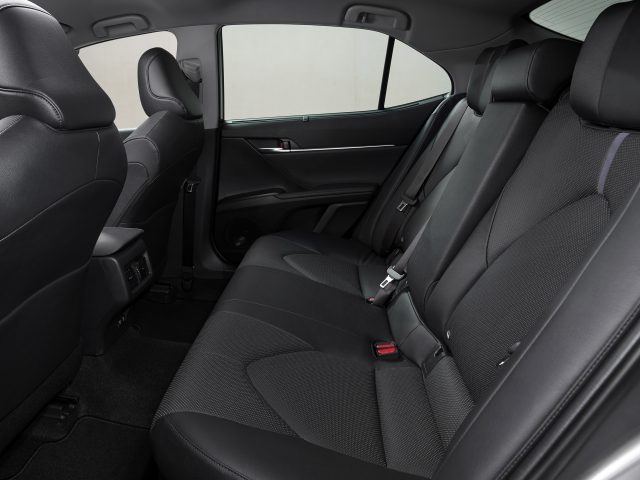 Binnenaanzicht van een Toyota Camry met de achterbank, met zwarte bekleding en een deurpaneel met raambediening.