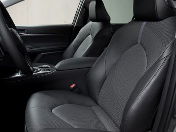 Binnenaanzicht van een Toyota Camry met de bestuurdersstoel en een deel van de passagiersstoel, voorzien van zwarte bekleding met gedetailleerde stiksels.