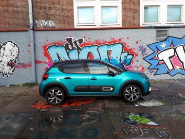 Een Citroën C3 geparkeerd in een met graffiti bedekte straat met kleurrijke muurschilderingen en gespoten grond.
