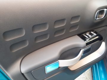 Binnenaanzicht van een Citroën C3-autodeur met een deurklink, elektrisch bediende raambediening en decoratieve panelen met geometrische patronen.