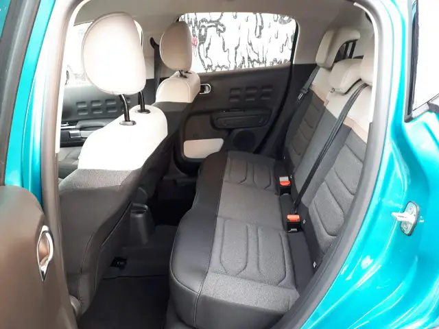 Binnenaanzicht van een Citroën C3 met de achterbank en deurpanelen, met grijze bekleding en veiligheidsgordels.