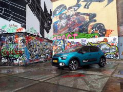 Een blauwe Citroën C3 geparkeerd in een steegje met kleurrijke graffiti en street art aan de muren.