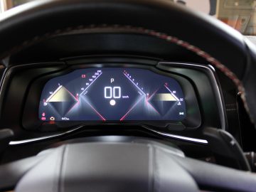 Digitaal autodashboard met een snelheidsmeter die 0 km/u aangeeft in een DS 9, geflankeerd door twee driehoekige grafische elementen, gezien vanuit het perspectief van de bestuurder.