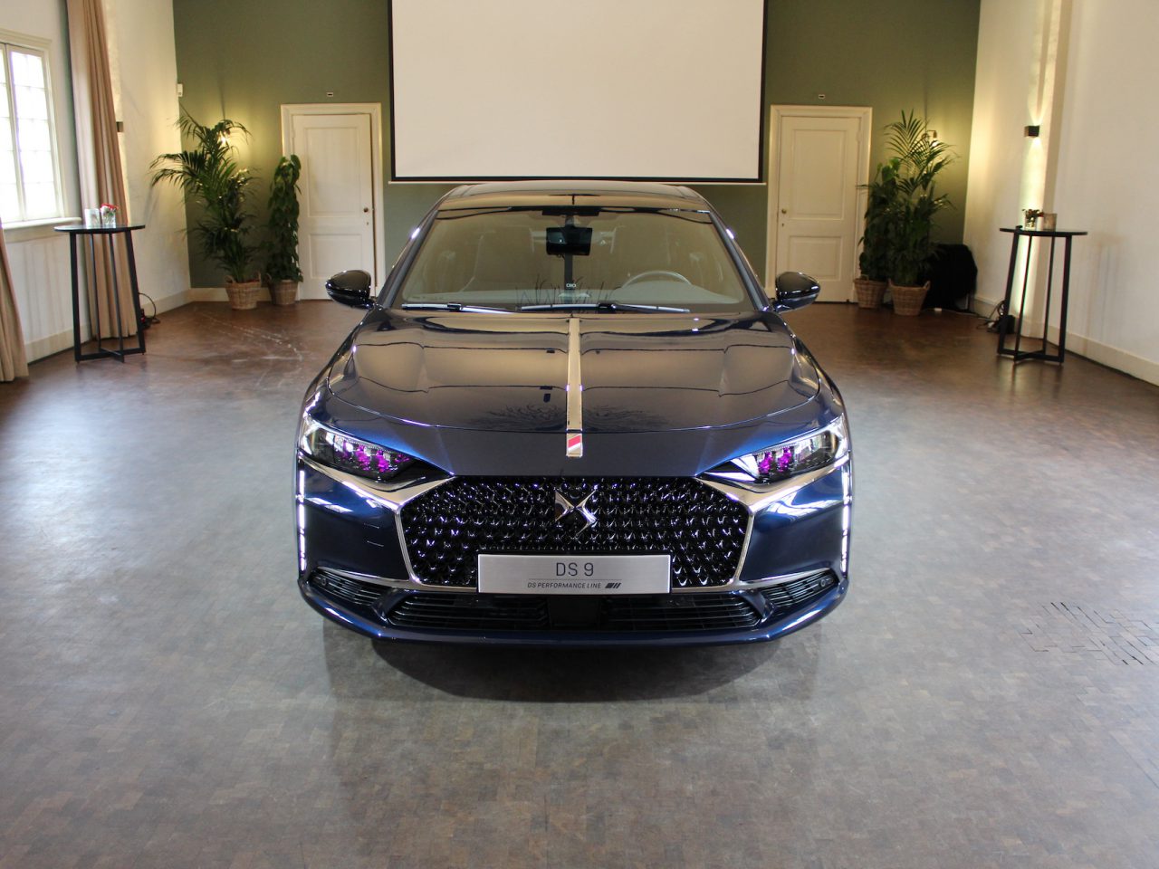 Een zwarte DS 9 sedan geparkeerd in een ruime kamer met grote ramen en een elegante inrichting.