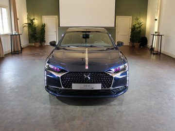 Een zwarte DS 9 sedan geparkeerd in een ruime kamer met grote ramen en een elegante inrichting.